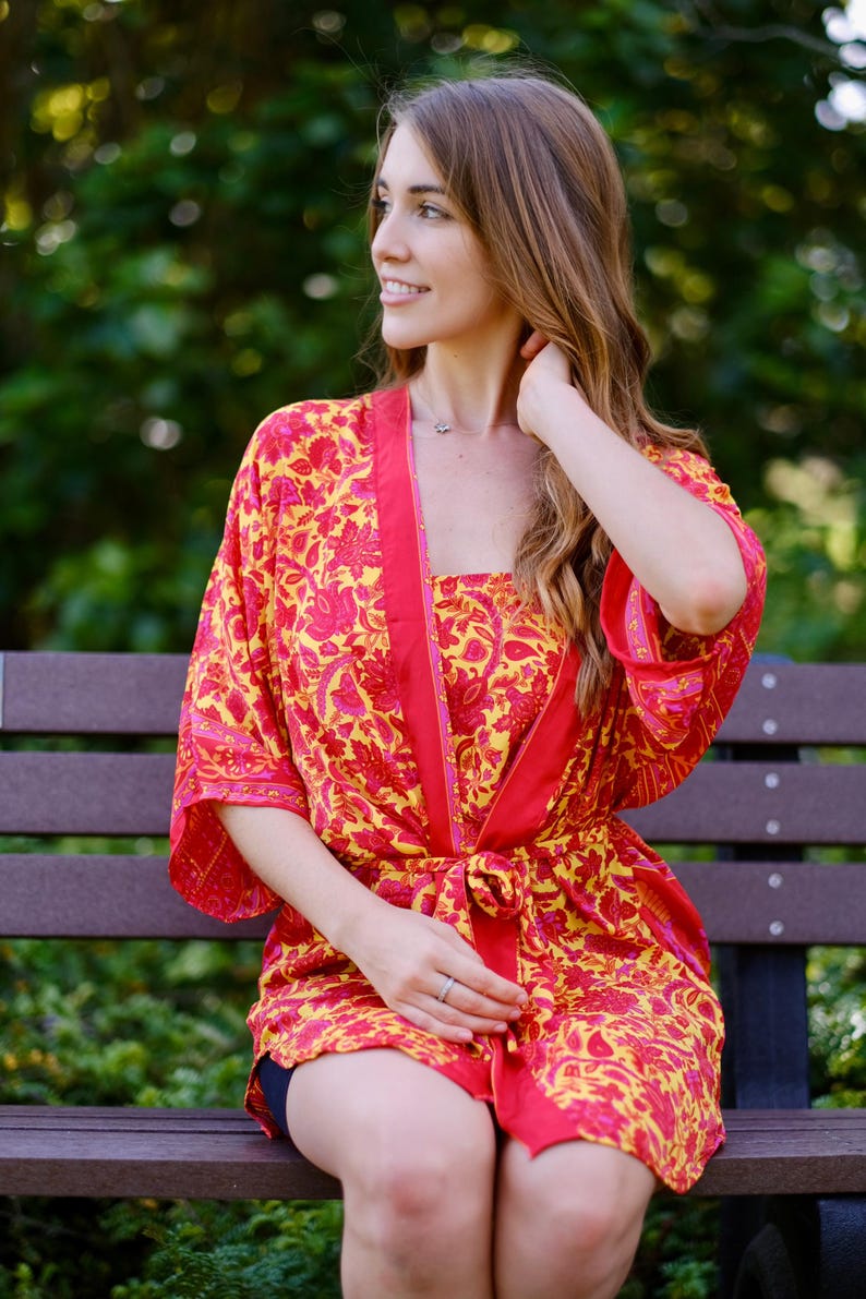 May include: A vibrant red and yellow floral print robe and matching top. The robe has a contrasting red trim and is tied at the waist. The outfit is made of a lightweight fabric, perfect for lounging.