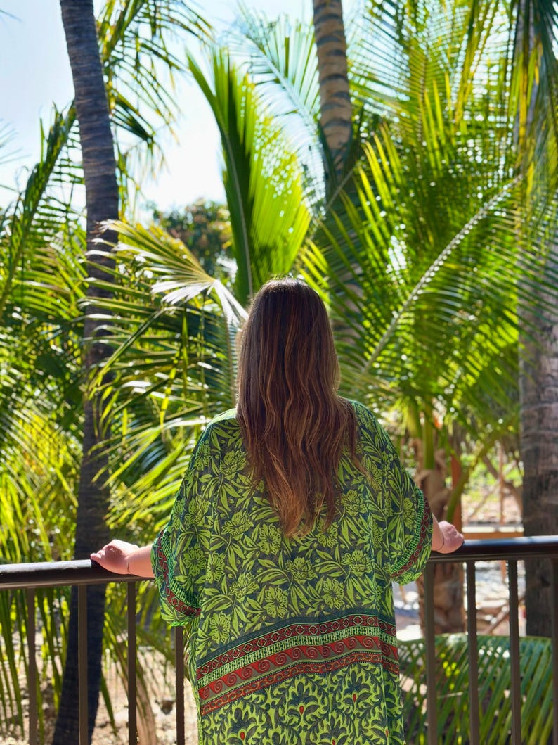Puede incluir: Una persona con un kimono verde con estampado floral, de pie en un balc&oacute;n con vistas a palmeras. El kimono tiene una base verde oscuro con dise&ntilde;os florales verde claro y detalles rojos y naranjas. La persona est&aacute; de espaldas.