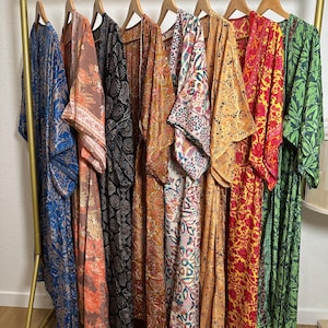 May include: A collection of colorful, patterned kimonos hanging on a gold clothing rack. The kimonos feature various designs in shades of blue, orange, black, yellow, red, and green. Each kimono is made of a lightweight fabric.