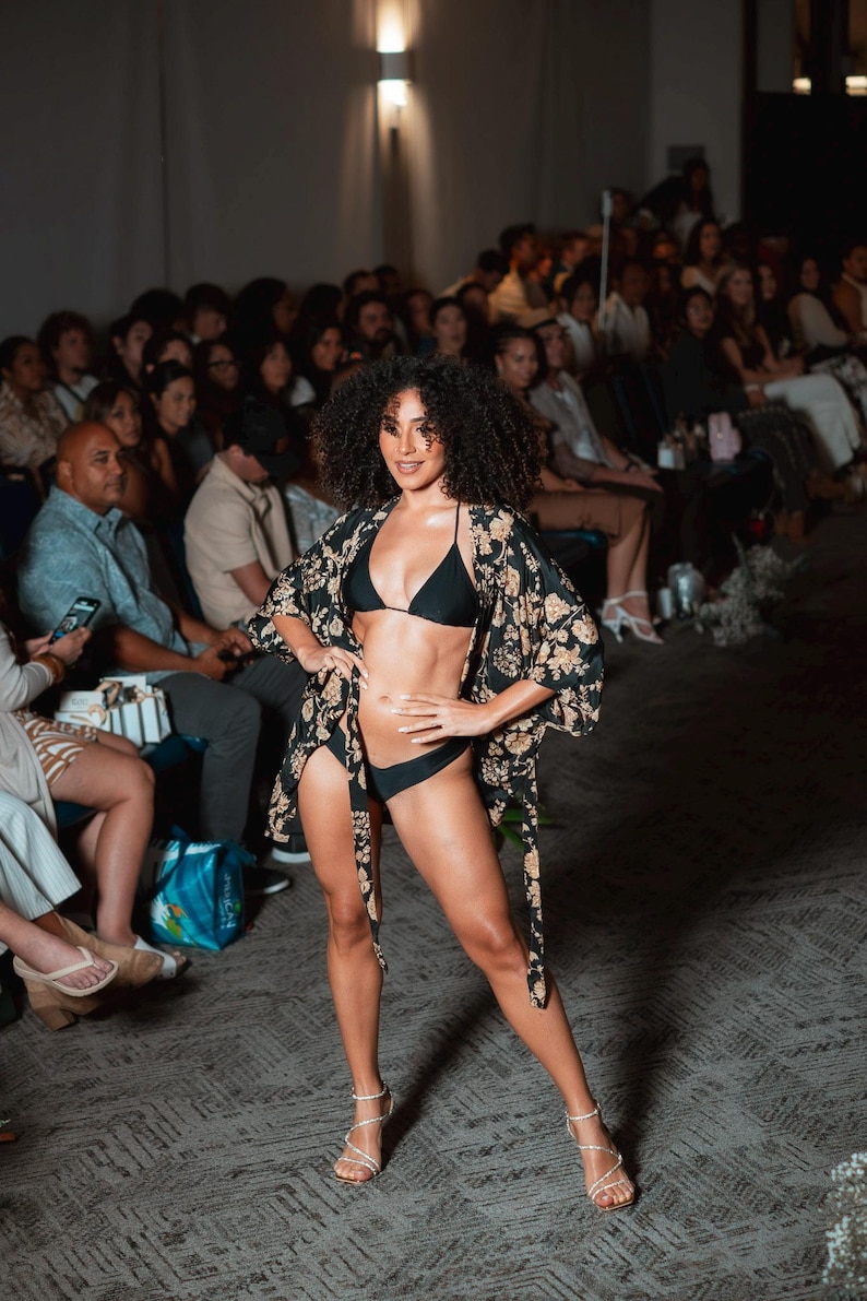 Pu&ograve; includere: Un set bikini nero composto da un top a triangolo e slip abbinati, abbinato a una vestaglia stile kimono nera con motivo floreale color marrone chiaro. La vestaglia presenta maniche larghe e apertura frontale, indossata con sandali a tacco alto.
