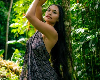 May include: A dark-colored sarong featuring a repeating circular mandala pattern in shades of blue, orange, and white. The fabric is draped over the body, secured at the neck, and displays a detailed geometric print across the entire surface area.