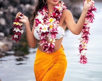 May include: A white strapless top paired with a vibrant orange sarong, accessorized with a long, multi-layered floral lei featuring deep red, pink, and white plumeria blossoms draped around the neck and held in both hands.