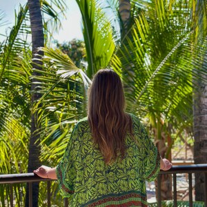 May include: A loose-fitting kimono-style garment featuring a vibrant lime green base with a dark green and red floral and paisley pattern. The fabric displays a wide horizontal border at the hem with intricate red and dark green decorative motifs.