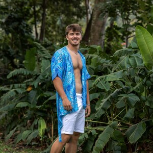May include: A bright blue, short-sleeved, open-front kimono-style shirt featuring a white and blue marbled pattern, paired with plain white shorts. The shirt has a loose, flowing fit with a straight hemline that falls below the waist.