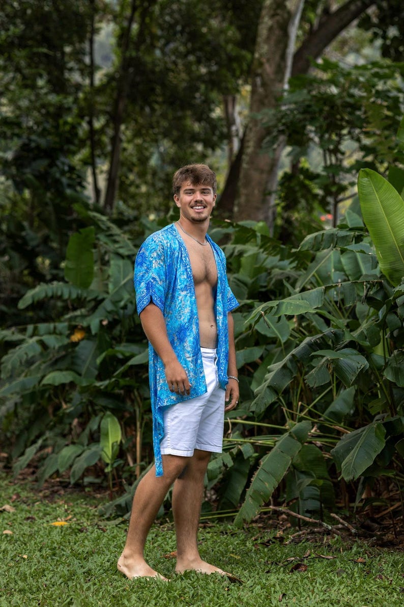 May include: A bright blue, short-sleeved, open-front kimono-style shirt featuring a white and blue marbled pattern, paired with plain white shorts. The shirt has a loose, flowing fit with a straight hemline that falls below the waist.