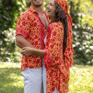 Puede incluir: Una camisa de manga corta con botones y un kimono abierto a juego, ambos con un vibrante estampado floral amarillo y rojo. El conjunto se combina con pantalones cortos blancos y una falda blanca, junto con un pañuelo floral a juego.
