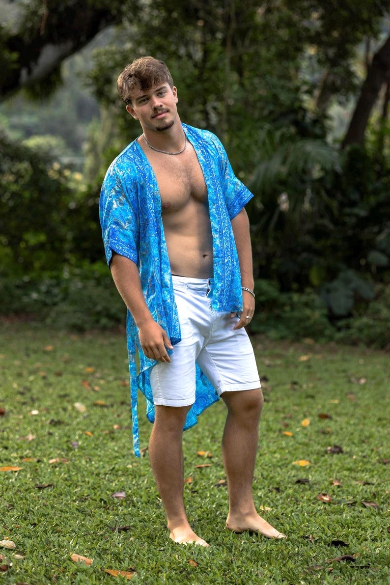 May include: A bright blue open-front kimono featuring a detailed paisley and floral pattern in shades of cyan and navy, paired with crisp white tailored shorts that reach above the knee, creating a coordinated ensemble for warm weather.