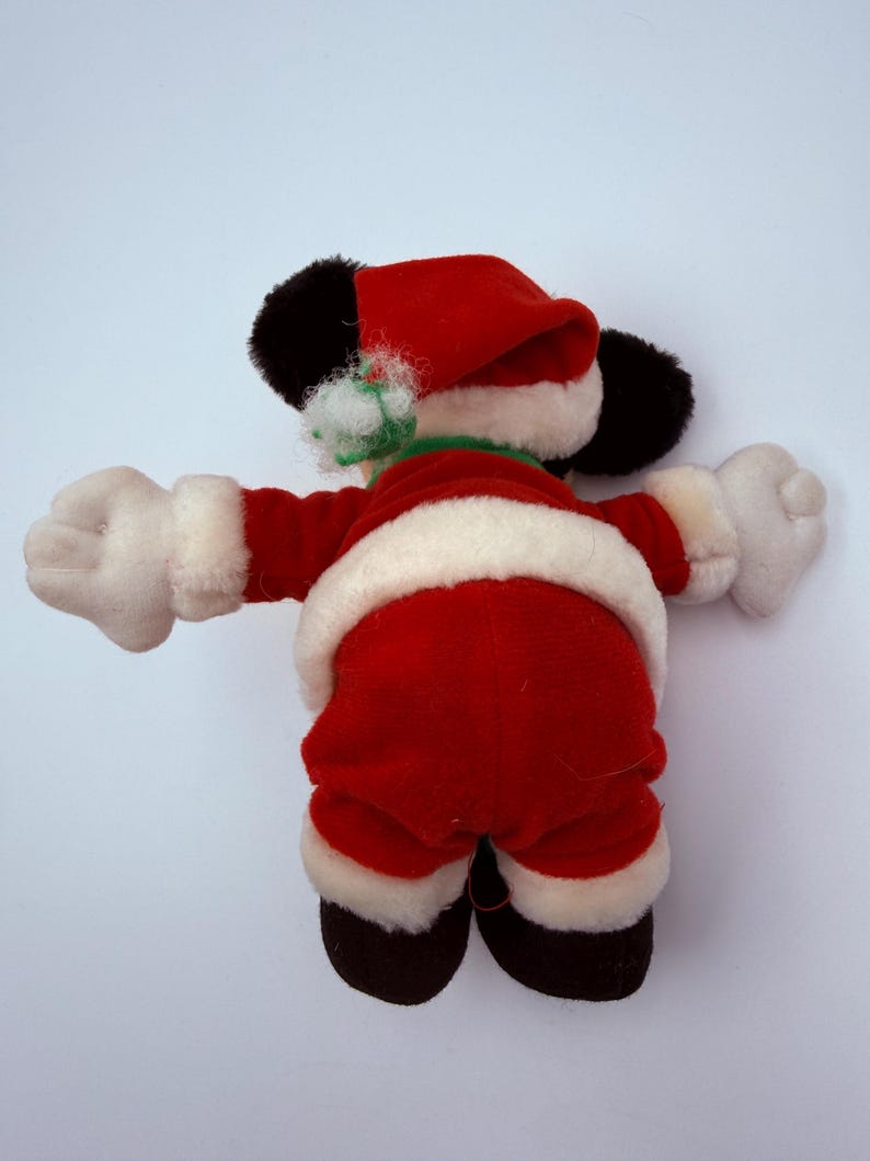 K&ouml;nnte beinhalten: Ein Pl&uuml;schtier, das als Weihnachtsmann verkleidet ist, von hinten gesehen. Das Spielzeug tr&auml;gt einen roten Anzug mit wei&szlig;em Besatz, einen passenden Hut und schwarze Schuhe. Das Spielzeug hat wei&szlig;e Handschuhe und schwarze Ohren.