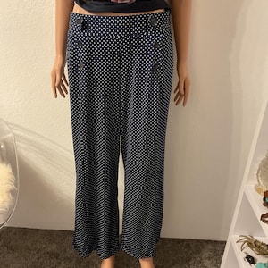 Puede incluir: Pantalones anchos azul marino con estampado de lunares blancos. Los pantalones tienen cintura alta y detalles de botones en los laterales. La modelo también lleva un top floral.