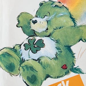 May include: A vintage Butterick pattern featuring the Good Luck Bear from Care Bears. The cover shows a green bear with a four-leaf clover on its belly, a rainbow, and the text "Good Luck Bear".