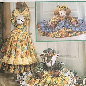 May include: A Simplicity Crafts sewing pattern envelope 8872 by Faith Van Zanten featuring illustrations of three fabric dolls dressed in sunflower-patterned outfits with ruffled skirts, bonnets, and hats, displayed in various poses.