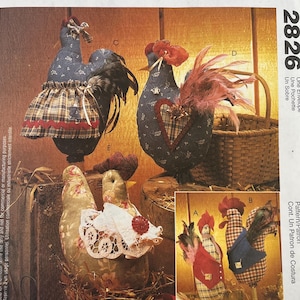 May include: A McCall's Crafts sewing pattern envelope, number 2826, featuring illustrations of five fabric chicken figures. The chickens are decorated with various textiles, including plaid skirts, lace collars, and feathers, displayed in a rustic setting.