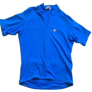 Puede incluir: Maillot de ciclismo azul brillante con cremallera corta y mangas cortas. Un pequeño logotipo es visible en el pecho. La tela parece ligera y transpirable, ideal para actividades deportivas.
