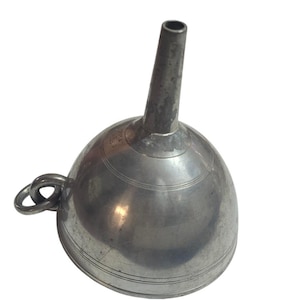 May include: A silver-toned metal funnel with a wide, rounded bowl and a narrow, tapered spout. The exterior surface features subtle horizontal engraved lines and a small metal ring attached to the side for hanging or storage purposes.