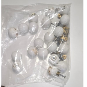 May include: A clear plastic bag filled with white ceramic cabinet knobs. The knobs are round with a speckled finish and brass hardware. Some knobs show signs of wear. The bag also contains screws for installation. Ideal for home improvement projects.