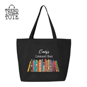 May include: Black tote bag with the text "Emily's Library Bag" and a colorful graphic of books. The bag has long black handles and the "Trend Tote" logo in the upper left corner.