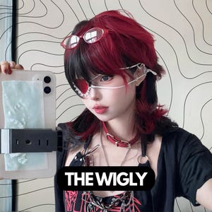 May include: A person with red and black hair, wearing glasses and a red choker, holds a phone with a protective case. The text "THE WIGLY" is displayed on a black banner. The background features a white wall with black curved lines.