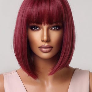 A woman with long, vibrant red hair styled in a short bob with bangs, wearing a pink dress.