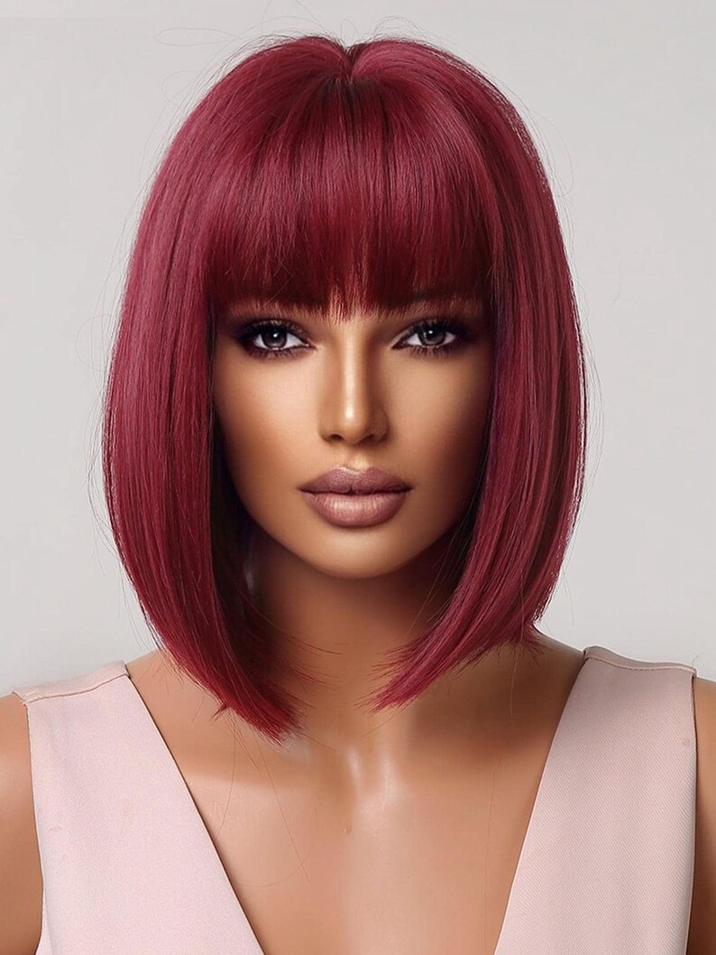 A woman with long, vibrant red hair styled in a short bob with bangs, wearing a pink dress.