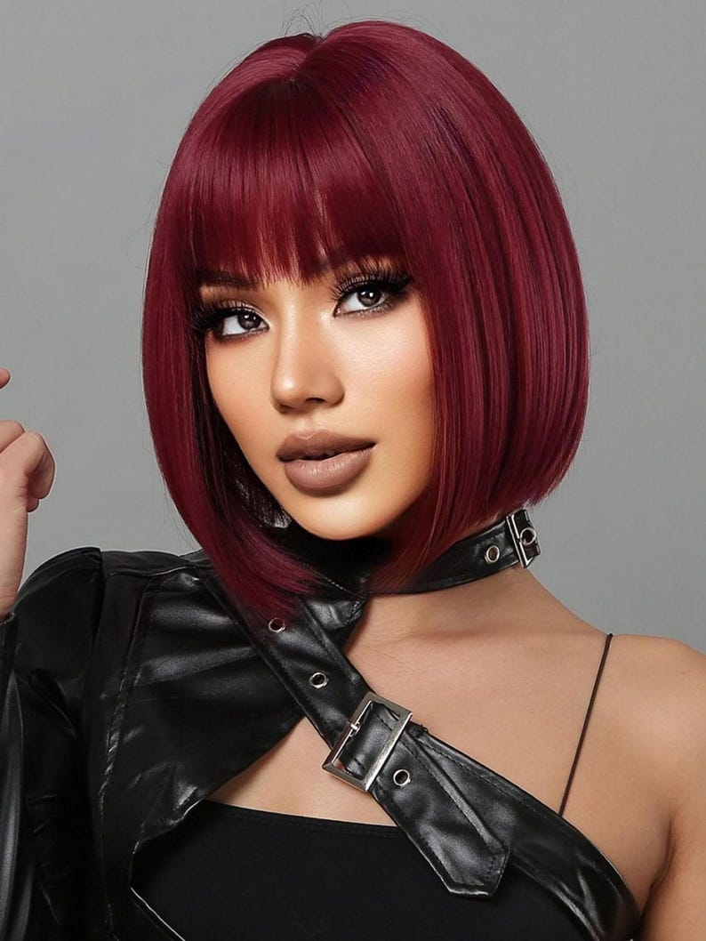 A woman with vibrant red hair styled in a short bob, wearing a black leather jacket and posing against a gray background.