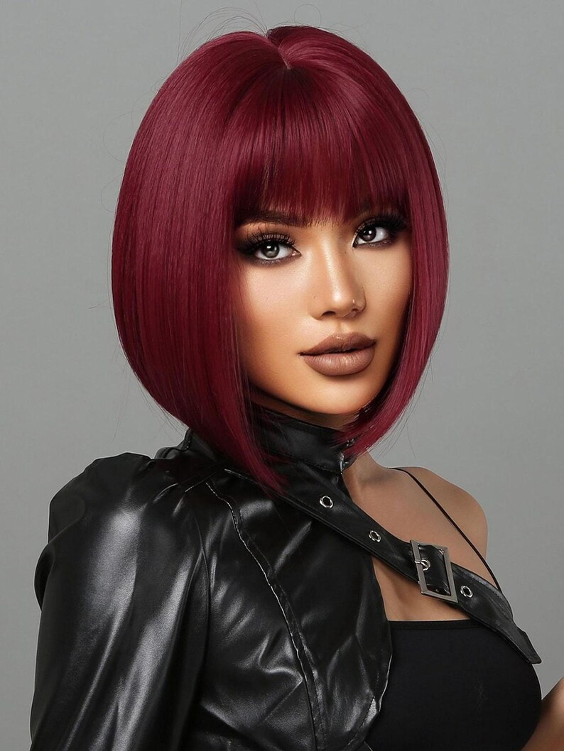 A woman with vibrant red hair styled in a short bob, wearing a black leather jacket and posing against a gray background.