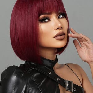 A woman with vibrant red hair styled in a short bob, wearing a black leather jacket and posing with her hand on her chin.