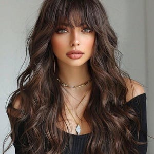 A woman with long, wavy brown hair and bangs, wearing a black top and a necklace, looking directly at the camera with a serious expression.