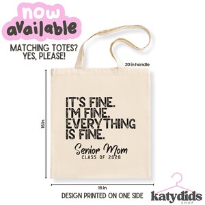 May include: Cream tote bag with black text: "IT'S FINE. I'M FINE. EVERYTHING IS FINE." and "Senior Mom CLASS OF 2026." The bag is 40.6 cm tall and 38.1 cm wide, with a 50.8 cm handle. The design is printed on one side.