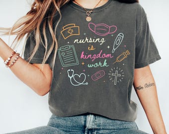 May include: Dark grey t-shirt with the text "nursing is kingdom work" and medical-themed graphics in neon colors. The design includes a nurse's hat, mask, thermometer, syringe, clipboard, stethoscope, bandage, and cross.