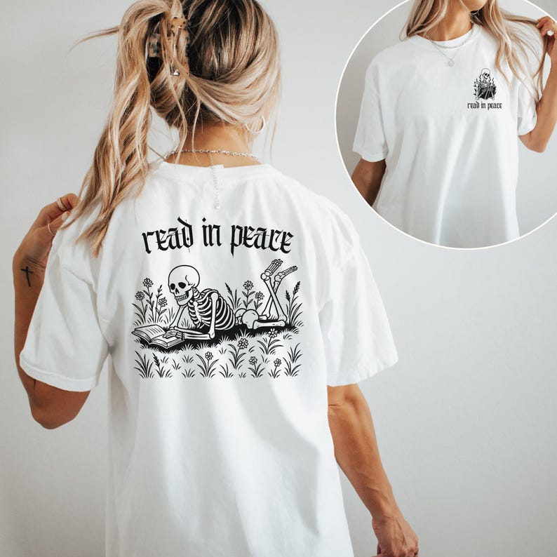 Puede incluir: Camiseta blanca con un gr&aacute;fico negro en la espalda que dice "read in peace". El gr&aacute;fico presenta un esqueleto leyendo un libro en un campo de flores y hierba. Una versi&oacute;n m&aacute;s peque&ntilde;a del gr&aacute;fico est&aacute; en la parte delantera.