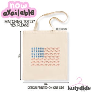 May include: A cream-colored tote bag with a design resembling the American flag, featuring blue drink glasses and red hot dogs. The bag is 16 inches tall and 15 inches wide, with a 20-inch handle. Text on the bag says "MATCHING TOTES? YES, PLEASE!" and "DESIGN PRINTED ON ONE SIDE."