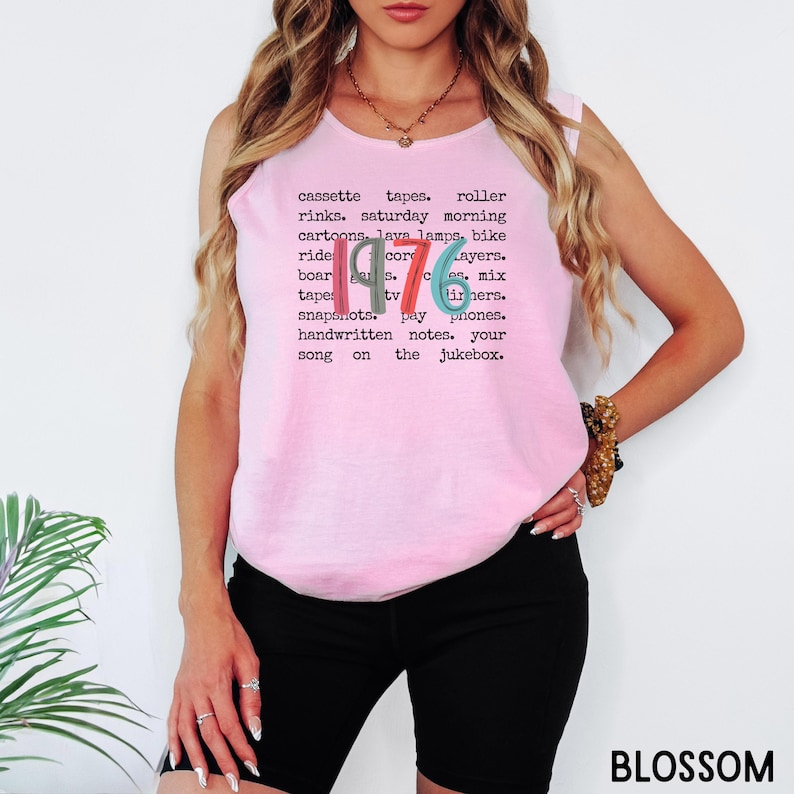 K&ouml;nnte beinhalten: Ein hellrosa &auml;rmelloses Shirt mit dem Wort "1976" in einem Retro-Schriftzug und einer Liste nostalgischer Begriffe. Das Wort "BLOSSOM" ist ebenfalls fett gedruckt unten rechts im Bild.