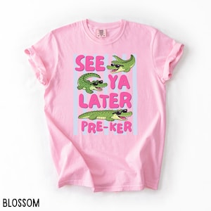 May include: Pink t-shirt with the text "SEE YA LATER PRE-KER" in pink and blue. The shirt features three green cartoon alligators wearing sunglasses. The word "BLOSSOM" is printed at the bottom.