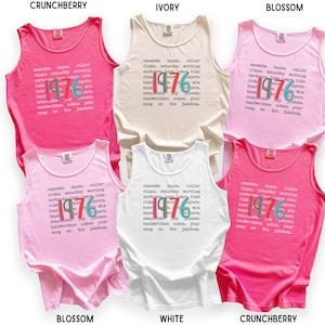 K&ouml;nnte beinhalten: Sechs Tanktops in den Farben Crunchberry, Ivory, Blossom und Wei&szlig;. Jedes Tanktop zeigt den Text "1976" mit einer Liste von W&ouml;rtern wie "Kassetten" und "Samstagmorgen".