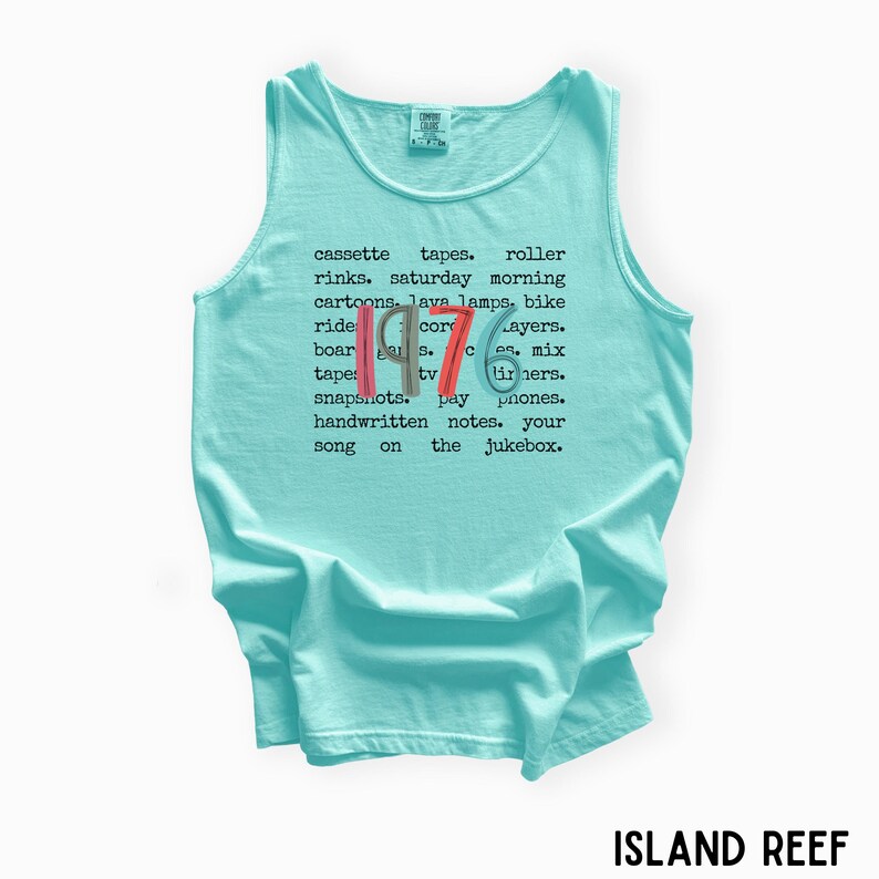 K&ouml;nnte beinhalten: Ein hellblaues Tanktop mit dem Wort "1976" in Rot, Wei&szlig; und Blau. Das Shirt zeigt eine Liste nostalgischer Gegenst&auml;nde und Phrasen aus den 1970er Jahren, wie Kassetten, Lavalampe und Rollschuhbahnen. Der Text "ISLAND REEF" befindet sich unten.