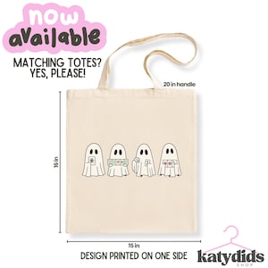 May include: A beige canvas tote bag featuring a graphic of four ghosts playing mahjong. The bag measures 16 inches in height and 15 inches in width, with a 20-inch handle. Text on the bag includes 'NOW AVAILABLE', 'MATCHING TOTES? YES, PLEASE!', and 'DESIGN PRINTED ON ONE SIDE'.