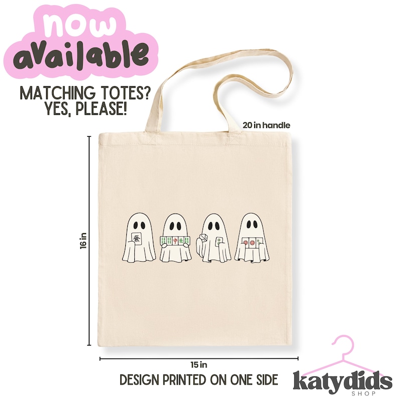 May include: A beige canvas tote bag featuring a graphic of four ghosts playing mahjong. The bag measures 16 inches in height and 15 inches in width, with a 20-inch handle. Text on the bag includes 'NOW AVAILABLE', 'MATCHING TOTES? YES, PLEASE!', and 'DESIGN PRINTED ON ONE SIDE'.
