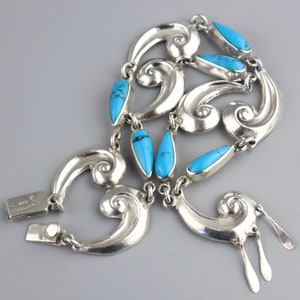 Puede incluir: Un collar de plata con piedras turquesas. El collar presenta una serie de formas estilizadas en espiral conectadas por eslabones. Piedras turquesas en forma de l&aacute;grima est&aacute;n intercaladas en el dise&ntilde;o. El cierre es visible.