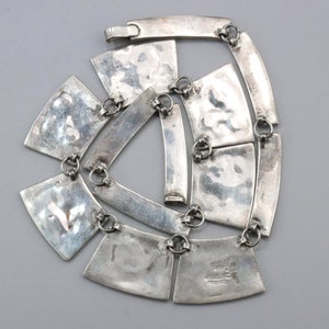 Op de afbeelding: Een zilveren ketting met een geometrisch ontwerp. De ketting is gemaakt van meerdere zilveren platen die met kleine zilveren ringen aan elkaar zijn verbonden. De platen zijn getextureerd en hebben een gehamerde afwerking. De ketting is 45,7 cm lang.