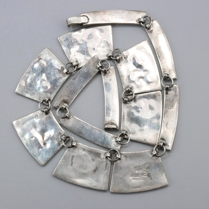 Op de afbeelding: Een zilveren ketting met een geometrisch ontwerp. De ketting is gemaakt van meerdere zilveren platen die met kleine zilveren ringen aan elkaar zijn verbonden. De platen zijn getextureerd en hebben een gehamerde afwerking. De ketting is 45,7 cm lang.