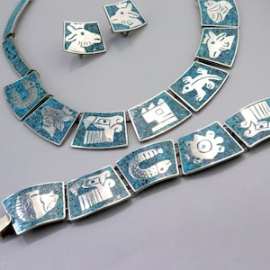Op de afbeelding: Een turquoise en zilveren ketting- en armbandset met geometrische ontwerpen. De sieraden hebben een herhalend patroon van gestileerde dieren en symbolen.