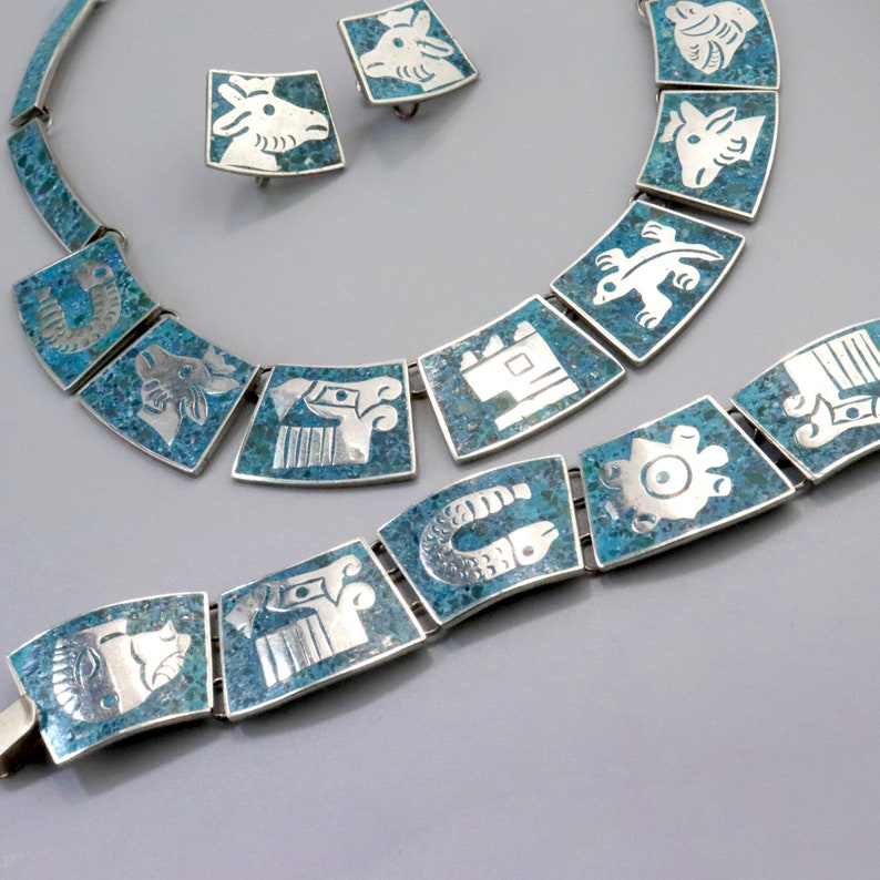 Op de afbeelding: Een turquoise en zilveren ketting- en armbandset met geometrische ontwerpen. De sieraden hebben een herhalend patroon van gestileerde dieren en symbolen.