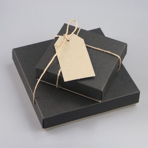Puede incluir: Tres cajas de regalo cuadradas negras de diferentes tama&ntilde;os est&aacute;n apiladas, con una etiqueta marr&oacute;n en blanco atada con hilo. Las cajas est&aacute;n dispuestas de forma anidada, con la caja m&aacute;s peque&ntilde;a encima.