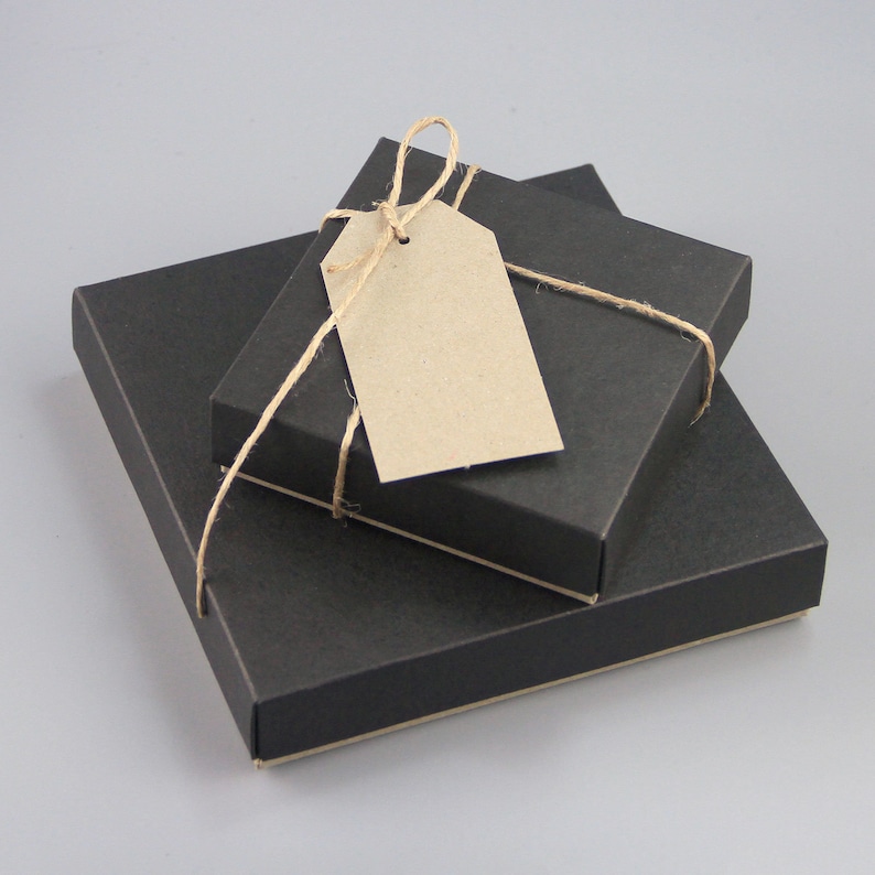 Puede incluir: Tres cajas de regalo cuadradas negras de diferentes tama&ntilde;os est&aacute;n apiladas, con una etiqueta marr&oacute;n en blanco atada con hilo. Las cajas est&aacute;n dispuestas de forma anidada, con la caja m&aacute;s peque&ntilde;a encima.