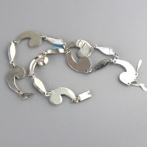 Puede incluir: Un collar de plata con un dise&ntilde;o &uacute;nico y fluido. El collar presenta formas estilizadas interconectadas, incluyendo elementos curvos y eslabones en forma de l&aacute;grima. Incorpora peque&ntilde;as piedras turquesas ovaladas. El cierre es de tipo gancho y barra.