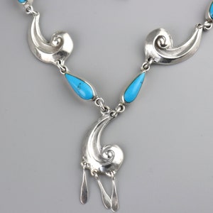 Puede incluir: Un collar plateado con una serie de formas arremolinadas estilizadas y piedras turquesas en forma de l&aacute;grima. El collar tiene un colgante con tres dijes colgantes alargados en forma de l&aacute;grima. Dise&ntilde;o sim&eacute;trico y elegante.