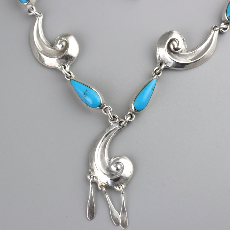Puede incluir: Un collar plateado con una serie de formas arremolinadas estilizadas y piedras turquesas en forma de l&aacute;grima. El collar tiene un colgante con tres dijes colgantes alargados en forma de l&aacute;grima. Dise&ntilde;o sim&eacute;trico y elegante.