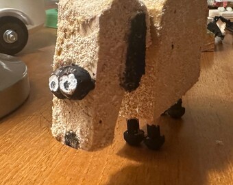 May include: A wooden animal sculpture of a dog with black painted eyes, ears, and legs. The dog is made of a light brown wood with a rough texture.