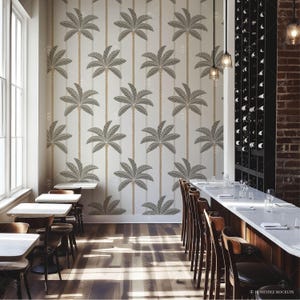 Pu&ograve; includere: Un interno di sala da pranzo con una parete bianca con un motivo ripetitivo di palme. La stanza ha un lungo tavolo di legno con sgabelli da bar e un bancone in marmo bianco. Il tavolo &egrave; apparecchiato con bicchieri e piatti.