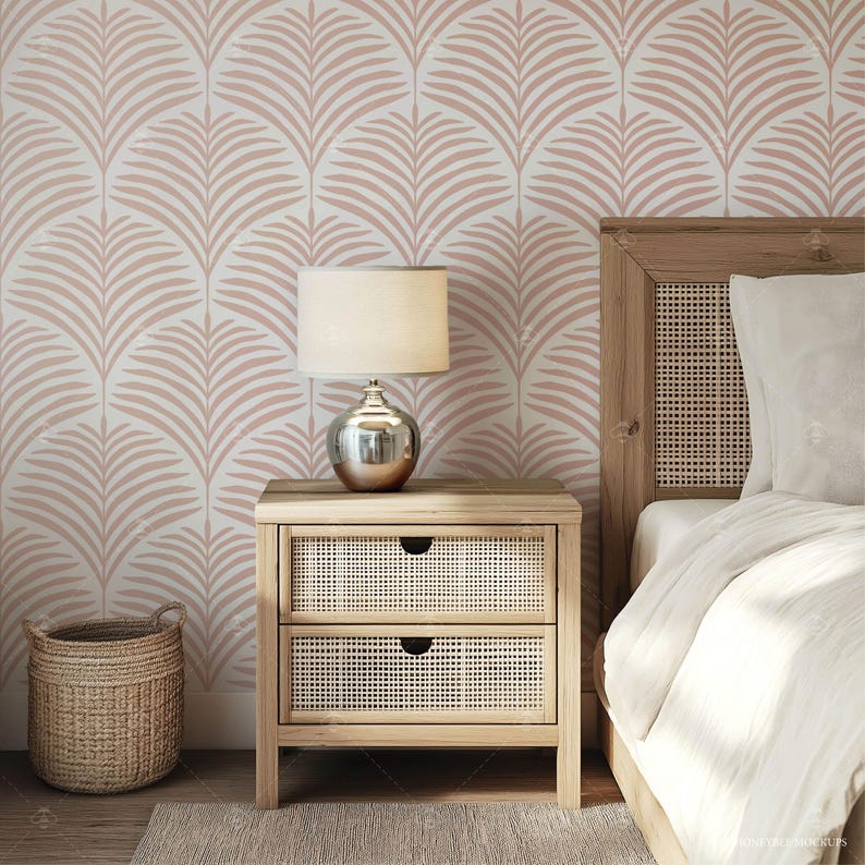 May include: A wooden nightstand with two drawers and a woven rattan front. A lamp with a white shade sits on top of the nightstand. The nightstand is in front of a wall with a pink and white palm leaf patterned wallpaper.